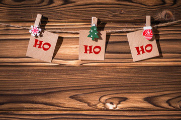 Ho ho ho phrase on little kraft paper stickers hanging on a rope on wooden clothespins. Santa Claus. Rustic Christmas decoration. Wooden boards background