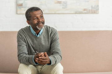 smiling african american man sitting on sofa and looking away