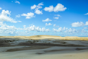 Sunny day landscape with dunes under sky and clouds.