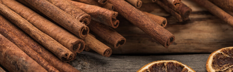 cinnamon sticks near dried citrus slices on wooden background, panoramic shot