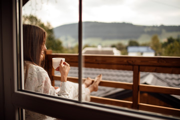 Young woman on the balcony holding a cup of coffee ore tea in the morning. She in hotel room...