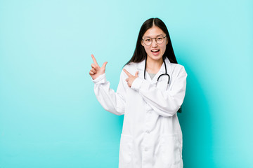 Young chinese doctor woman pointing with forefingers to a copy space, expressing excitement and...