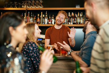 Handsome caucasian bartender giving beer on house to customers.