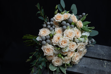 Beautiful wedding bouquet of bushy cream rose, eucalyptus, Brunei, Pittosporum and Lisianthus on a black background.