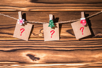 Question mark on little kraft paper stickers hanging on a rope on wooden clothespins. Santa Claus.  Rustic Christmas decoration.  Wooden boards background