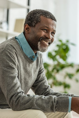 cheerful african american man in grey pullover smiling while looking away