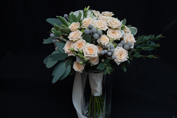 Beautiful wedding bouquet of bushy cream rose, eucalyptus, Brunei, Pittosporum and Lisianthus on a black background.