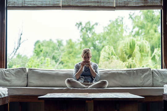 Mature woman having coffee while sitting on sofa at home