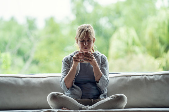 Smiling mature woman having coffee while sitting on sofa at home