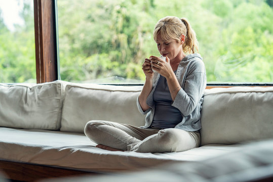 Smiling mature woman having coffee while sitting on sofa at home