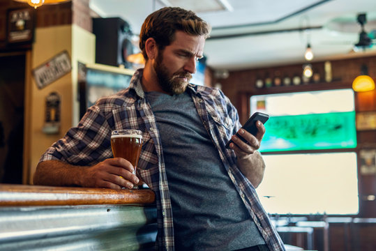 Serious man with beer glass using smartphone at bar counter