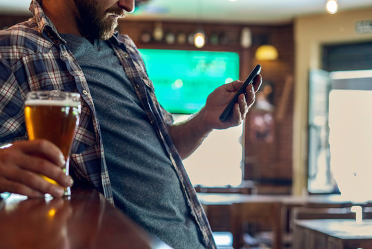 Mid section of man with beer glass using smartphone at bar counter
