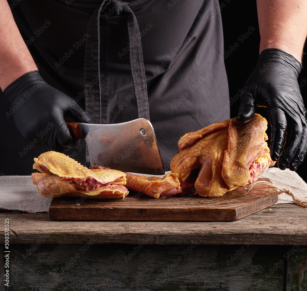 Wall mural chef in black uniform and latex gloves chopping raw chicken into pieces