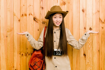 Young chinese traveler woman makes scale with arms, feels happy and confident.