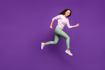 Fototapeta na wymiar Full length body size photo of cheerful hurriyng urgent girl flying forward with light speed wearing green trousers smiling toothily running jumping up isolated over purple vivid color background