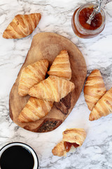 Fresh homemade croissants with jam and a cup of coffee over marble background  Image shot from top view. 
