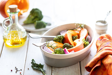 Traditional autumn pumpkin dishes. Grilled roasted pumpkin with spices, olive oil, herbs, broccoli and onions. On a baking sheet, on a rustic wooden white background. copy space