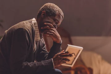 Deurstickers senior, depressed african american man looking at photo frame © LIGHTFIELD STUDIOS