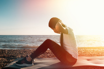 Concept of sport and healthy lifestyle. Woman in sportswear is training on the Mat. In the background, a rocky shore and the sea. Outdoor. Copy space. Light