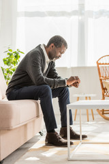 depressed african american man sitting on sofa with bowed head