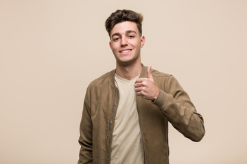Young caucasian man wearing a brown jacket smiling and raising thumb up