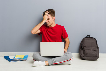 Young student man sitting on his house floor holding a laptop