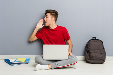 Young student man sitting on his house floor holding a laptop
