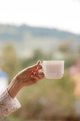 Girl's hand holding a cup of coffee in the morning, mountain view behind, relax and freedom day. Lifestyle Concept.