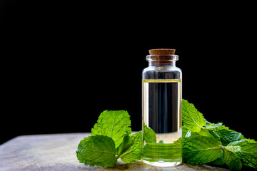 Peppermint essential oil bottle with fresh mint leaves, placed on a wooden plate and have a black background.