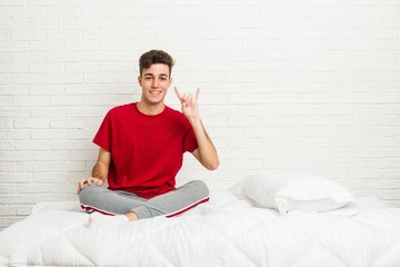 Young teenager student man on the bed showing a horns gesture as a revolution concept.