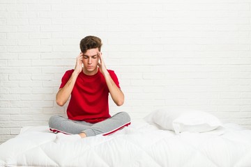 Obraz premium Young teenager student man on the bed touching temples and having headache.