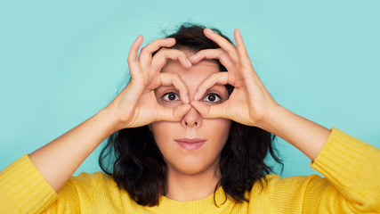 funny young woman holding fingers near eyes on a blue background