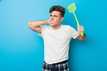 Teenager caucasian man wearing pyjamas and holding a flyswatter