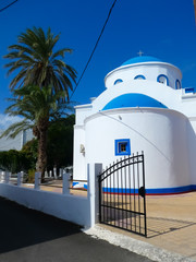 Typical Greek Orthodox Church white and blue on a beautiful sunny day with a blue sky beside a palm tree