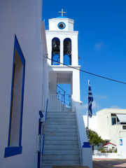 Fototapeta na wymiar Stepped front of a white and blue Orthodox church with bell tower and Greek flag