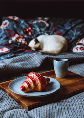 Cherry croissant with a cup of espresso on a wooden tray in a bed. The concept of cozy morning at home.