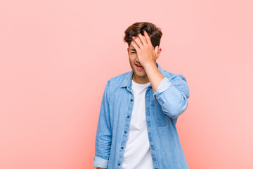 young handsome man laughing and slapping forehead like saying d‚Äôoh! I forgot or that was a...