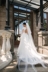 Back view of Gorgeous bride stand on the stairs in elegant wedding dress with bouquet of white flowers in her wedding day