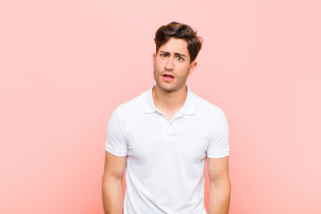 young handsome man feeling puzzled and confused, with a dumb, stunned expression looking at...