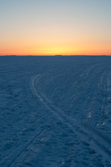 Frozen ski tracks on sea-ice with the setting sun coloring the sky with orange and pink in Pori, Finland