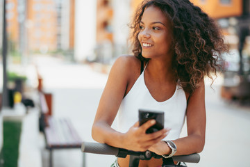 Beautiful african woman outdoors. Young woman on her electric scooter using phone