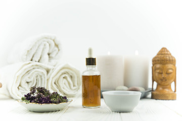 Obraz na płótnie Canvas Spa treatment bottle of natural organic oil essence serum collagen. Towel, aromatic candles, flowers, massage brush and Buddha on white background. Copy space for text. Beautiful woman hands. Oil drop