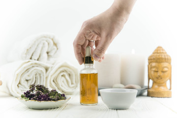 Spa treatment bottle of natural organic oil essence serum collagen. Towel, aromatic candles, flowers, massage brush and Buddha on white background. Copy space for text. Beautiful woman hands. Oil drop