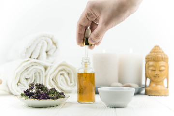 Spa treatment bottle of natural organic oil essence serum collagen. Towel, aromatic candles, flowers, massage brush and Buddha on white background. Copy space for text. Beautiful woman hands. Oil drop