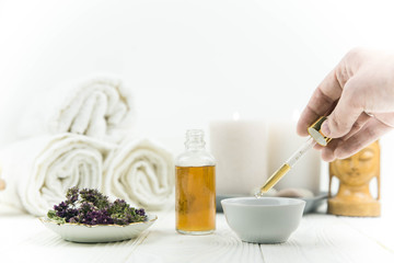 Spa treatment bottle of natural organic oil essence serum collagen. Towel, aromatic candles, flowers, massage brush and Buddha on white background. Copy space for text. Beautiful woman hands. Oil drop