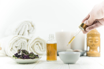 Spa treatment bottle of natural organic oil essence serum collagen. Towel, aromatic candles, flowers, massage brush and Buddha on white background. Copy space for text. Beautiful woman hands. Oil drop