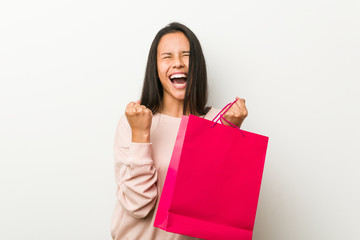 Fototapeta na wymiar Young hispanic woman holding a shopping bag cheering carefree and excited. Victory concept.