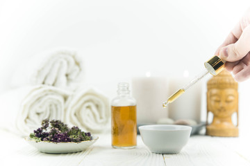 Spa treatment bottle of natural organic oil essence serum collagen. Towel, aromatic candles, flowers, massage brush and Buddha on white background. Copy space for text. Beautiful woman hands. Oil drop