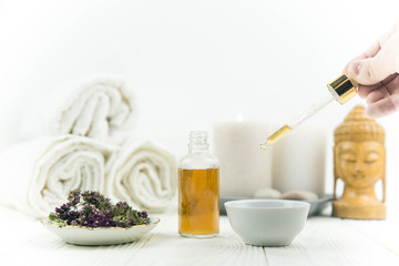 Spa treatment bottle of natural organic oil essence serum collagen. Towel, aromatic candles, flowers, massage brush and Buddha on white background. Copy space for text. Beautiful woman hands. Oil drop