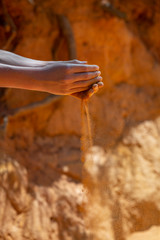 Hands of young boy holding yellow red sand from national park Roussillion, France while dust powder falls through fingers